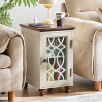 White bedside end table with glass cabinet door, dark handles, and charging cords